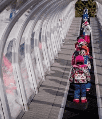 groupe de jeunes élève en train d'emprunter le tapis sous un tunnel en verre sur staiton de ski luz ardiden